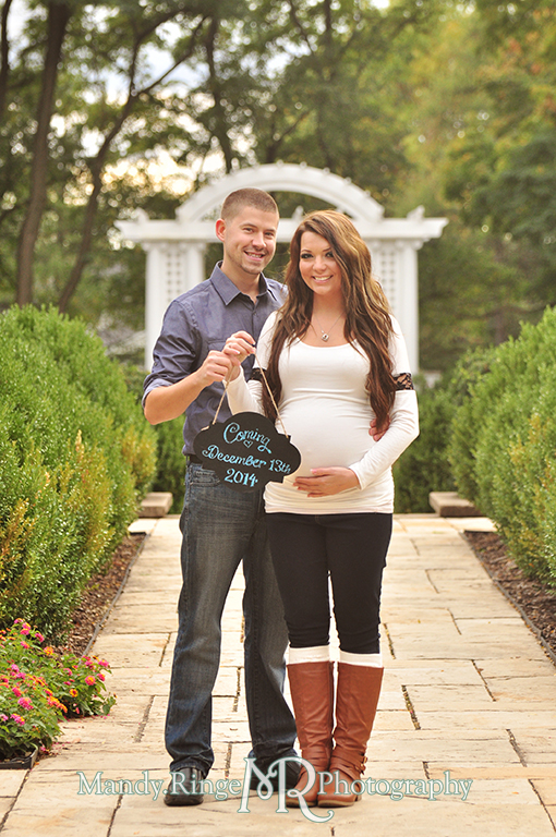 Man and pregnant woman posing in front of a white arch holding a chalkboard sign announcing the due date // Maternity portraits // Hurley Gardens - Wheaton, IL // by Mandy Ringe Photography