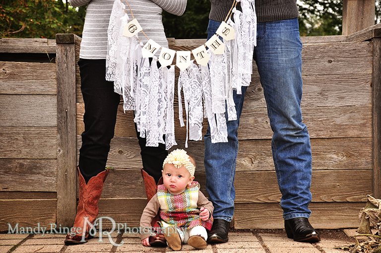 6 month old baby girl portraits // Baby sitting on the ground by parents feet with parents holding a lace rag garland and a banner that says 6 months // Cantigny Gardens - Wheaton, IL // by Mandy Ringe Photography