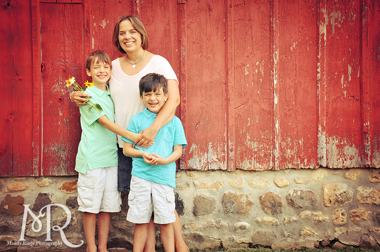 Family of three standing in front of a red barn // Leroy Oaks // by Mandy Ringe Photography