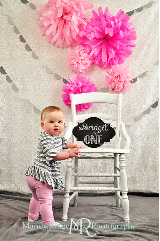 Baby girl's first birthday photo shoot. Sitting on a white chair. Pink tissue paper poms, gray paint chip garland // Pink, gray and white birthday // by Mandy Ringe Photography