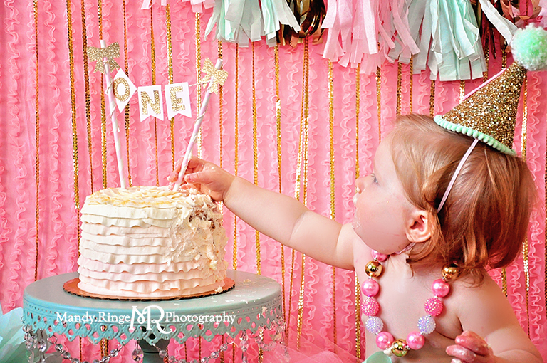 Pink, gold, and mint first birthday // Smash cake session // Tassle garland, tissue poms, pink ruffle fabric backdrop, gold sequin strands // St Charles, IL // by Mandy Ringe Photography