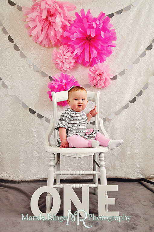 Baby girl's first birthday photo shoot. Sitting on a white chair with letters spelling out ONE. Pink tissue paper poms, gray paint chip garland // Pink, gray and white birthday // by Mandy Ringe Photography