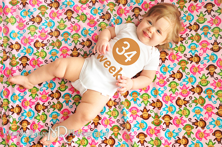 Weekly photos of a baby girl for the first year // Laying on a fabric backdrop, photoshopped numbers on white onesies // by Mandy Ringe Photography