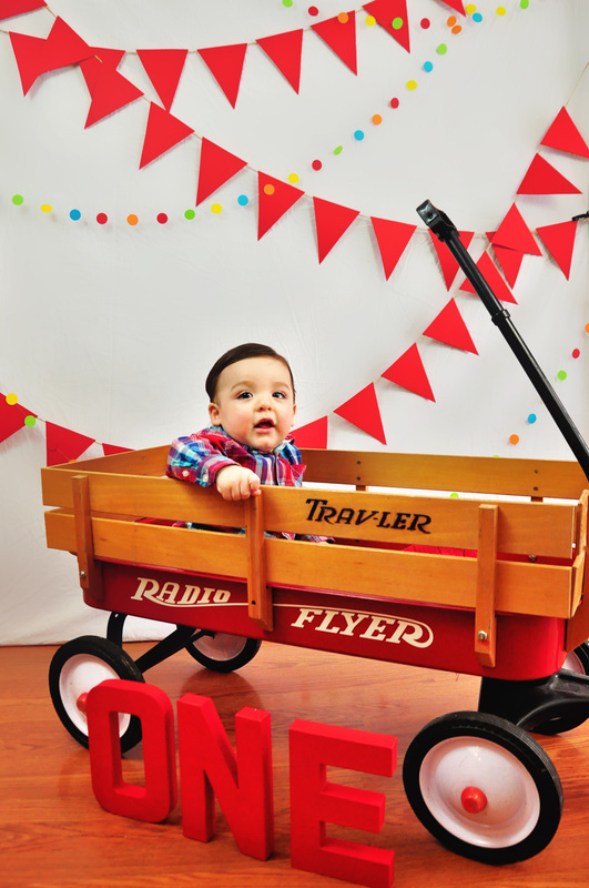 Boy's first birthday // Sitting in a Radio Flyer wagon // Red pennant banners, multicolor dot garland, wagon, ONE letters // by Mandy Ringe Photography
